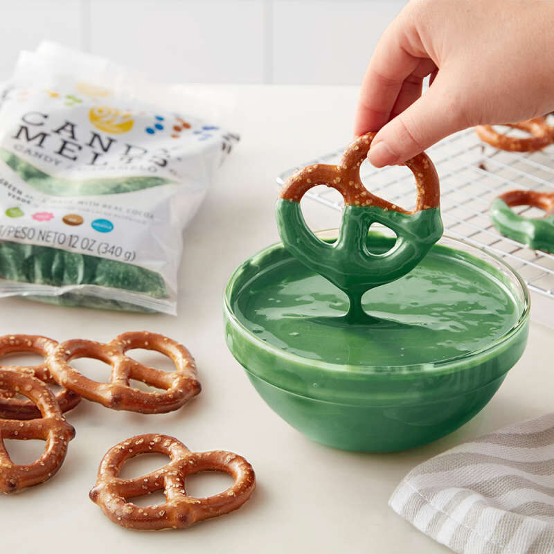 Dipping Pretzels into bowl of melted dark green Candy Melts Candy image number 3