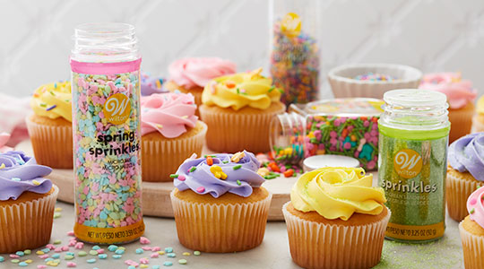 Pink, yellow, white, light green, purple sprinkle packets and cupcakes topped with sprinkles